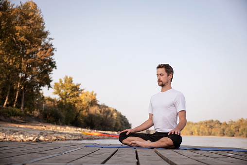 Mid aged man practicing yoga outdoor. Caucasian man using yoga mat and doing lotus pose on nature.