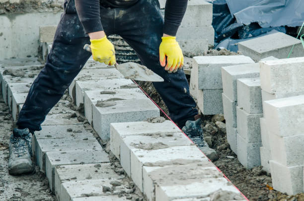 ciężko pracujący murarz układający bloczki betonowe na belce fundamentowej na nowym osiedlu mieszkaniowym. walka z kryzysem mieszkaniowym poprzez budowę bardziej przystępnych cenowo domów - cenowo zdjęcia i obrazy z banku zdjęć