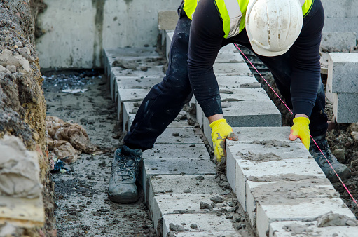 Hard working bricklayer laying concrete blocks on top of concrete foundation ground beam on new residential housing site. Fight housing crisis by building more affordable houses concept