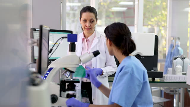 Female lab technician analyzing a sample and talking to female doctor asking for something at the hospital’s lab