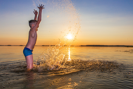 European boy bathes in the lake. The sun is shining in the background.