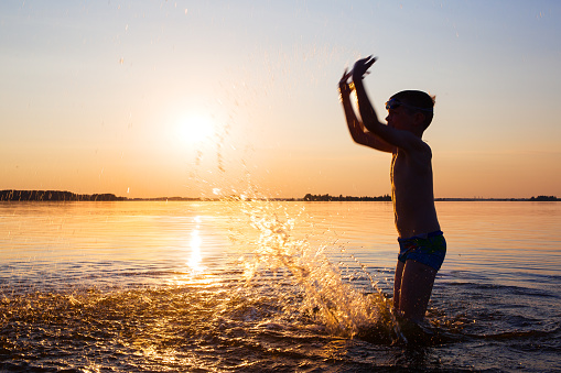 Photo of a person in motion. Silhouette of a man against the background of the sun. A child splashes water in the lake.