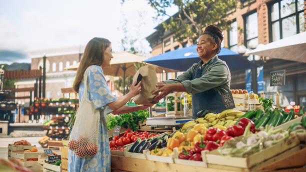 istock Beautiful Female Customer Buying Sustainable Organic Vegetables From a Joyful Black Female Farmer on a Sunny Summer Day. Successful Street Vendor Managing a Farm Stall at an Outdoors Eco Market 1934731631