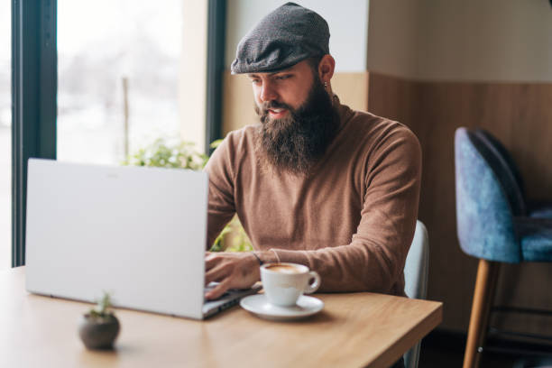 istock Bearded smiling man sitting in cafe, drinking fresh coffee and using laptop 1934733334