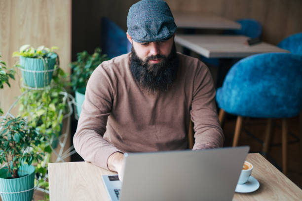 istock Bearded smiling man sitting in cafe, drinking fresh coffee and using laptop 1934733848
