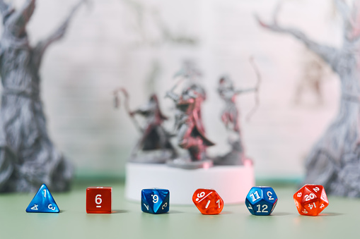 Role playing tabletop game and board game hobby concept. Blue and red dice place for adventure story TTRPG with adventurer miniatures background. Creation with fantasy narrative at home.