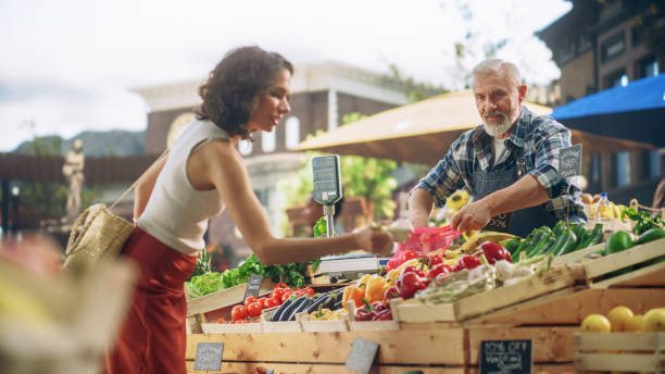istock Cheerful Local Farmer Running a Small Business, Selling Sustainable Farm Fruits and Vegetables. Happy Middle Aged Male Welcoming a Female Shopper to Try Tomatoes and Other Organic Produce From a Farm 1934736068