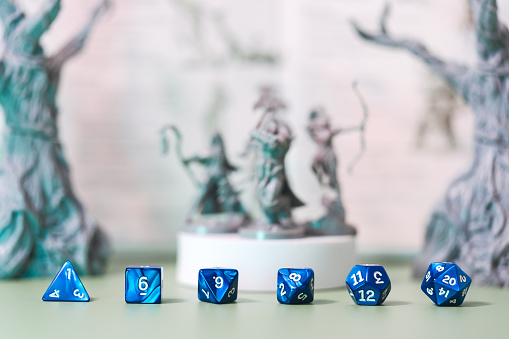 Role playing tabletop game and board game hobby concept. Blue dice place for adventure story TTRPG with adventurer miniatures background. Creation with fantasy narrative at home.