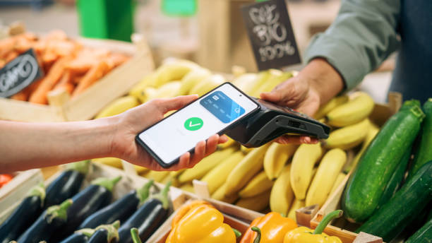 istock Digital Banking Concept: Shopper Using Cellphone with Contactless Payment Technology to Pay for Natural Goods at a Farmers Market. Street Vendor Holding an Electronic Payment and a Card Reader Device 1934741641