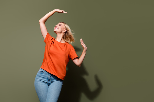 Photo portrait of attractive young woman fluttering hair raise hands dressed stylish orange clothes isolated on khaki color background.