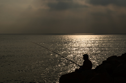 Person fishing, sunset at sea