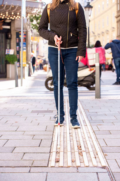 Cropped shot of a visually impaired woman with white cane in hand walking through pedestrian crossing in the city stock photo