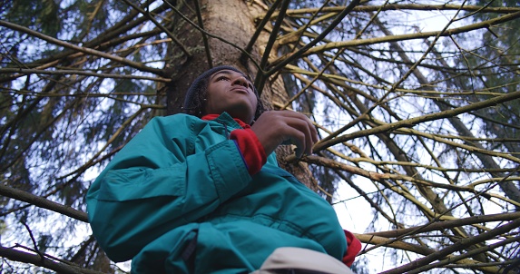 African American teenager having snack in the woods during tourist trip or trek in autumn. Young hiker or traveler resting in camp after long hike in the mountains. Tourism and active leisure concept.