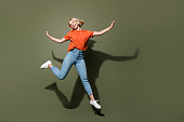 Full size body view of lady wear orange t shirt denim jeans jumping flying air hands up playing childish isolated on khaki color background