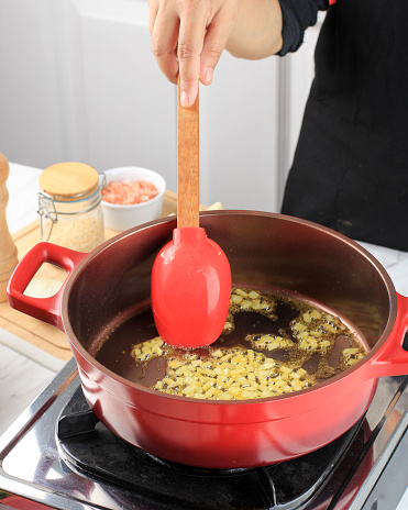 Chef is stirring white chopped onions being fried sauteed in a red cast iron dutch oven