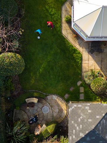 Drone aerial view of a father and Jason playing football together in the family garden. Other family members watch from aside located in Middlesborough, England.