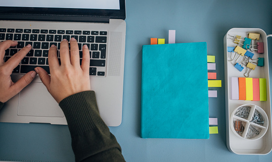 A professional engages in digital tasks at a laptop, complemented by a notebook with colorful sticky note markers for efficient workflow management.