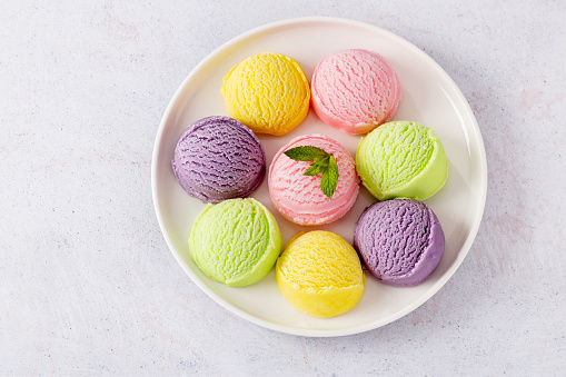 Pastel colored ice cream scoops on white plate, top view. Different flavor and color ice cream served on plate, copy space.