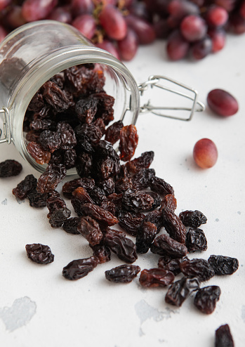 Dark dried sweet raisins in glass jar on light background.