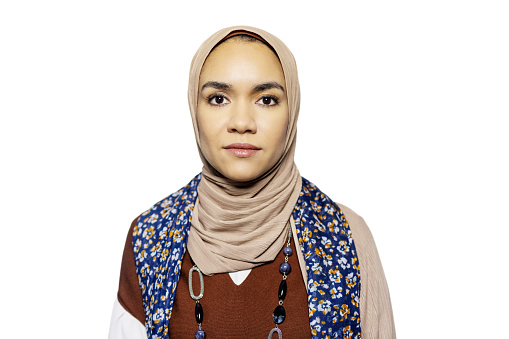 Portrait of young Islamic woman with blank expression on white background. Muslim female with hijab staring at camera in studio.