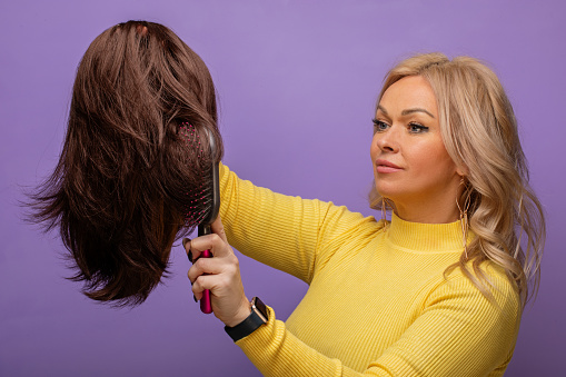 Portrait of female hairdresser holding hairbrushes and tools in yellow and purple