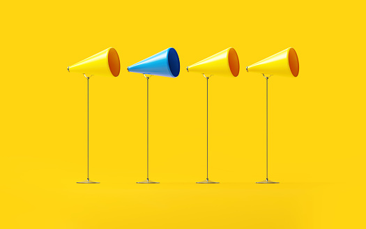 Blue and yellow megaphones on yellow background. Standing out from the crowd concept. Horizontal composition.