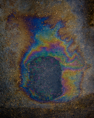 A multi coloured oil spill from a leaking oil sump on a concrete road.