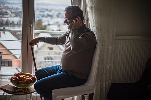 An elderly man is alone at home, using a smartphone