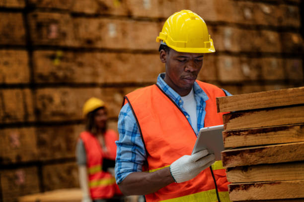 istock African worker carpenter wearing safety uniform and hard hat working and checking the quality of wooden products at workshop manufacturing. man and woman workers wood in dark warehouse industry. 1934935307