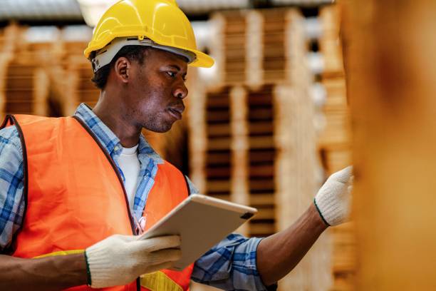 istock African worker carpenter wearing safety uniform and hard hat working and checking the quality of wooden products at workshop manufacturing. man and woman workers wood in dark warehouse industry. 1934941684