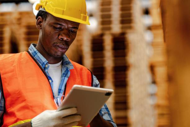 istock African worker carpenter wearing safety uniform and hard hat working and checking the quality of wooden products at workshop manufacturing. man and woman workers wood in dark warehouse industry. 1934942775