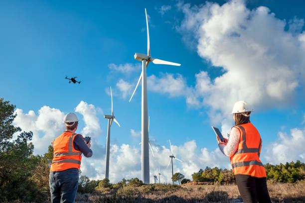 istock Engineer mechanic using drone for inspection in a windmill farm park. Female engineer at wind turbines farm with digital tablet 1934957080