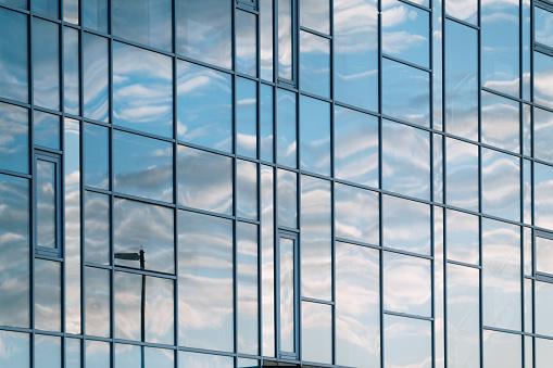 Full frame image showing the glass facade of a modern office building, with clouds reflected