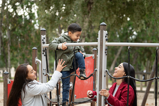Kid having fun with his mother in a playground. Lesbian women mothers with their son playing in a jungle gym.