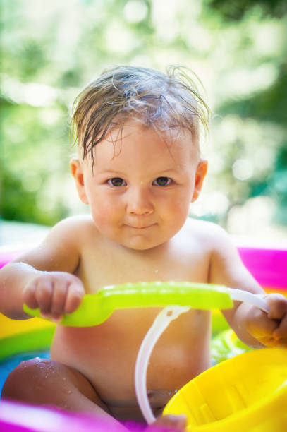 маленький мальчик сидит в бассейне в саду и играет с водными игрушками - swimming pool one baby boy only toddler image type стоковые фото и изображения