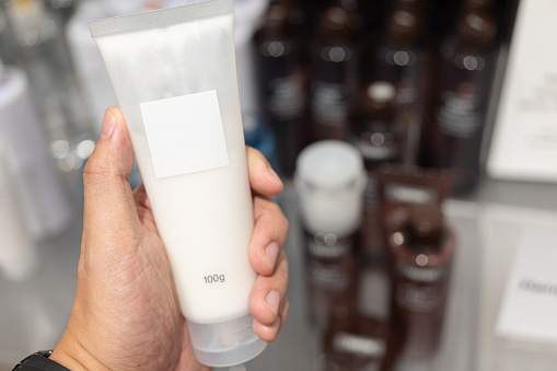 Cream in a tube on hand at cosmetic store. Dermatologist hands holding blank cosmetic skincare bottle. Foam dispenser for face care. Container with body lotion.