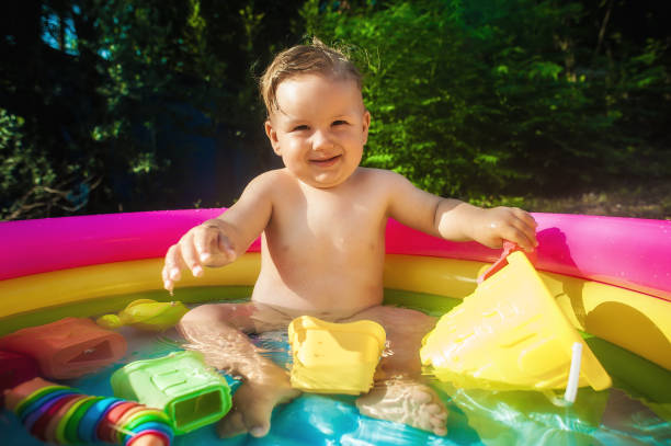 baby boy sitting in a pool at the garden and playing with water toys - swimming pool one baby boy only toddler image type стоковые фото и изображения