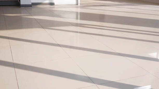 istock Sunlight and long shadow pattern of glass and aluminum wall frame on surface of beige ceramic tile floor inside of room 1935010966
