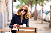 Attractive blond haired woman sitting at a table outside a cafe and using her smartphone