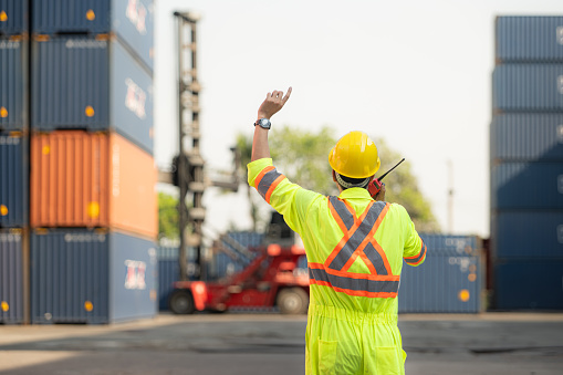 Workers in the import and export industry use walkie talkies to communicate with drivers of reach stacker containers in an empty container warehouse.