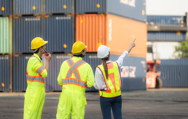 istock Group of workers in the import and export industry use walkie talkies to communicate with drivers of reach stacker containers in an empty container warehouse. 1935043802