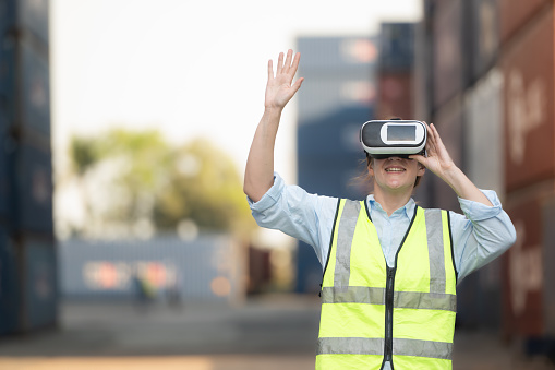 Woman wearing virtual reality headset or 3d glasses to control work in a container warehouse.