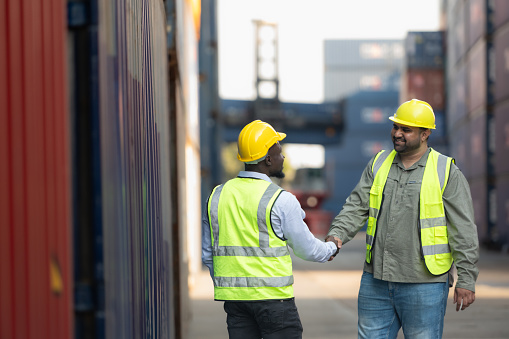 Both of workers in a container storage yard greeting each other during breaks in front of container warehouse,