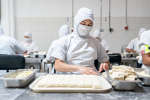 Latin American employee working at an industrial bakery making pastries and wearing protective workwear - food industry concepts