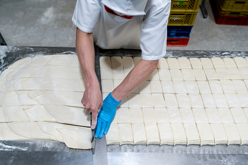 Baker cutting the dough while working at an industrial bakery - food industry concepts