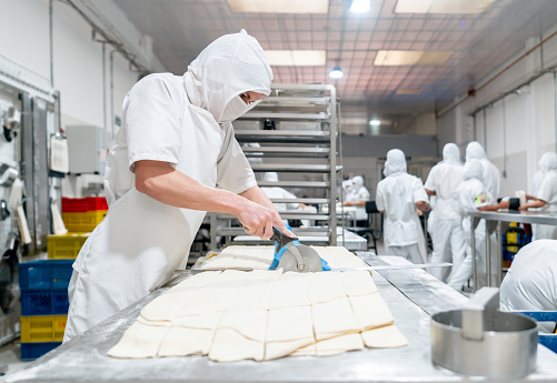 Latin American baker cutting the dough while working at an industrial bakery - food industry concepts
