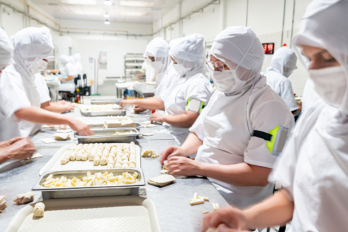 Group of Latin American employees working at a food processing plant rolling pastries - food industry concepts