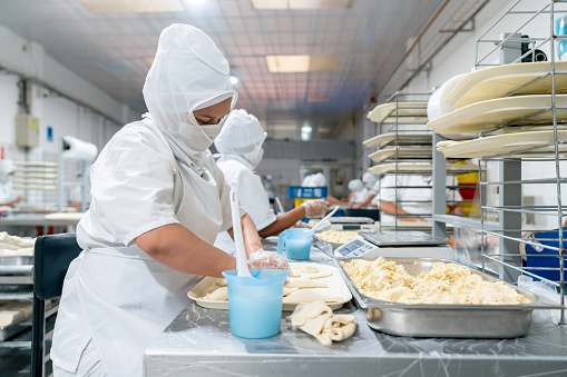 Latin American employee working at an indsutrial bakery making pastries while kneading the down - production line concepts