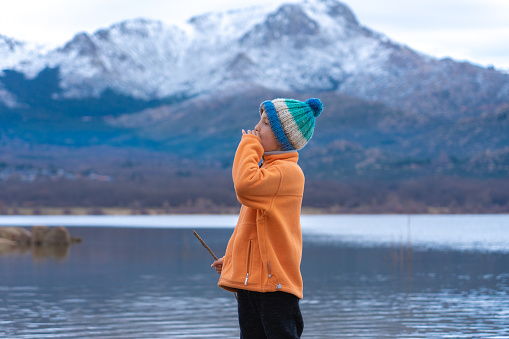 Boy screaming outdoors in winter with a landscape of a lake and snowy mountains