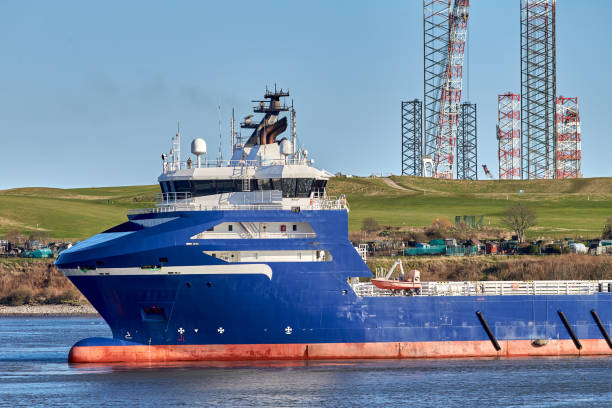 Blue platform supply vessel navigating in port with mountains on the background.